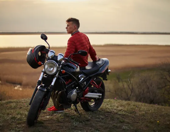 Chico apoyado en una moto viendo el atardecer
