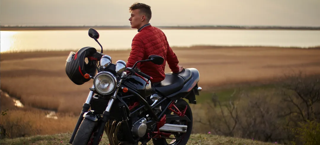 Chico apoyado en una moto viendo el atardecer