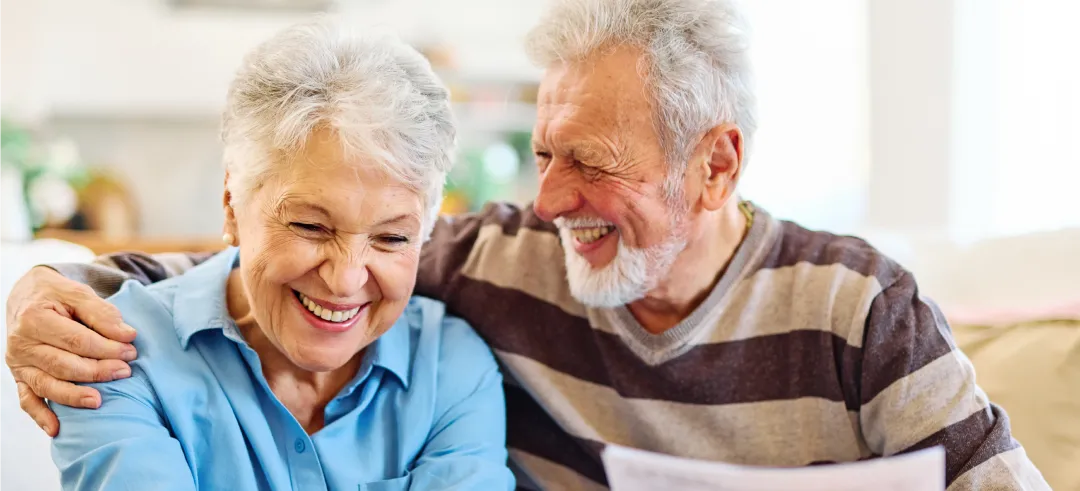 An adult couple laughing whilst sitting on the sofa