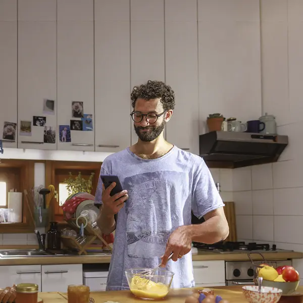 chico con el móvil en una mano y batiendo huevos con la otra